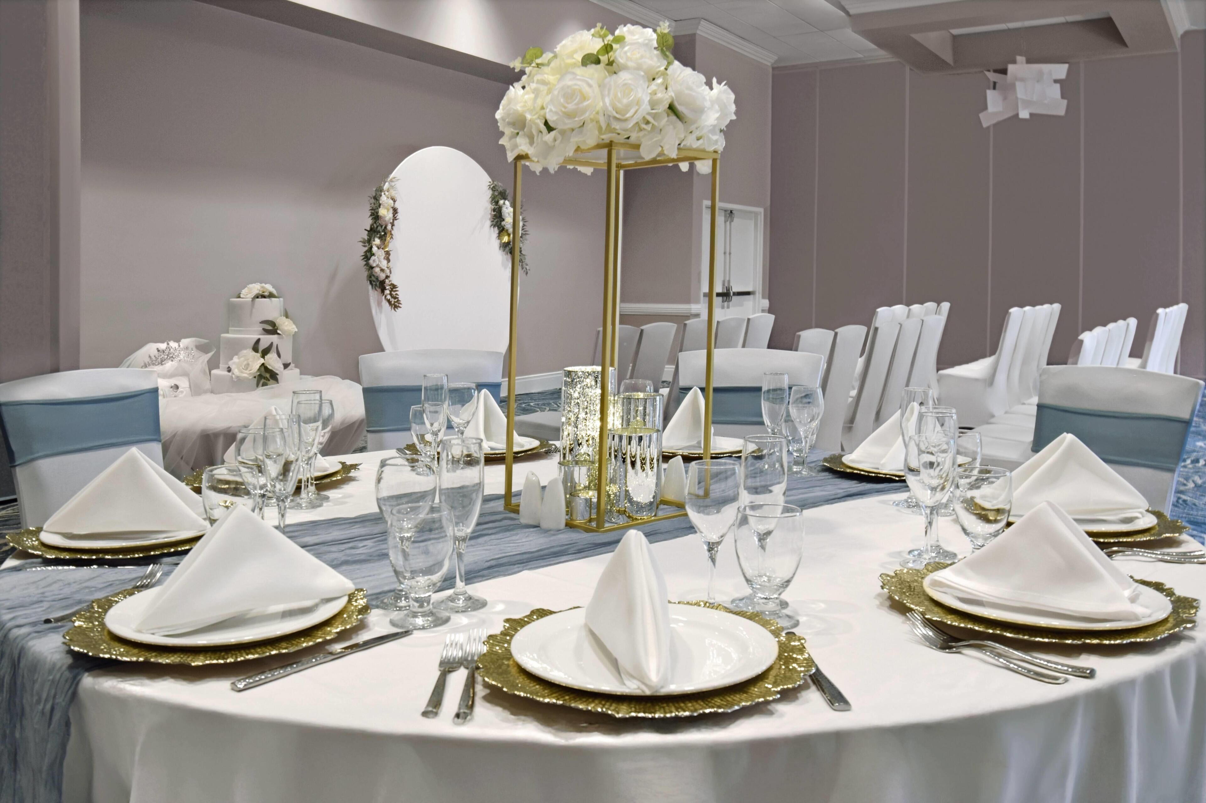 A round table set for a formal event with white tablecloths, gold-rimmed plates, and clear glassware.