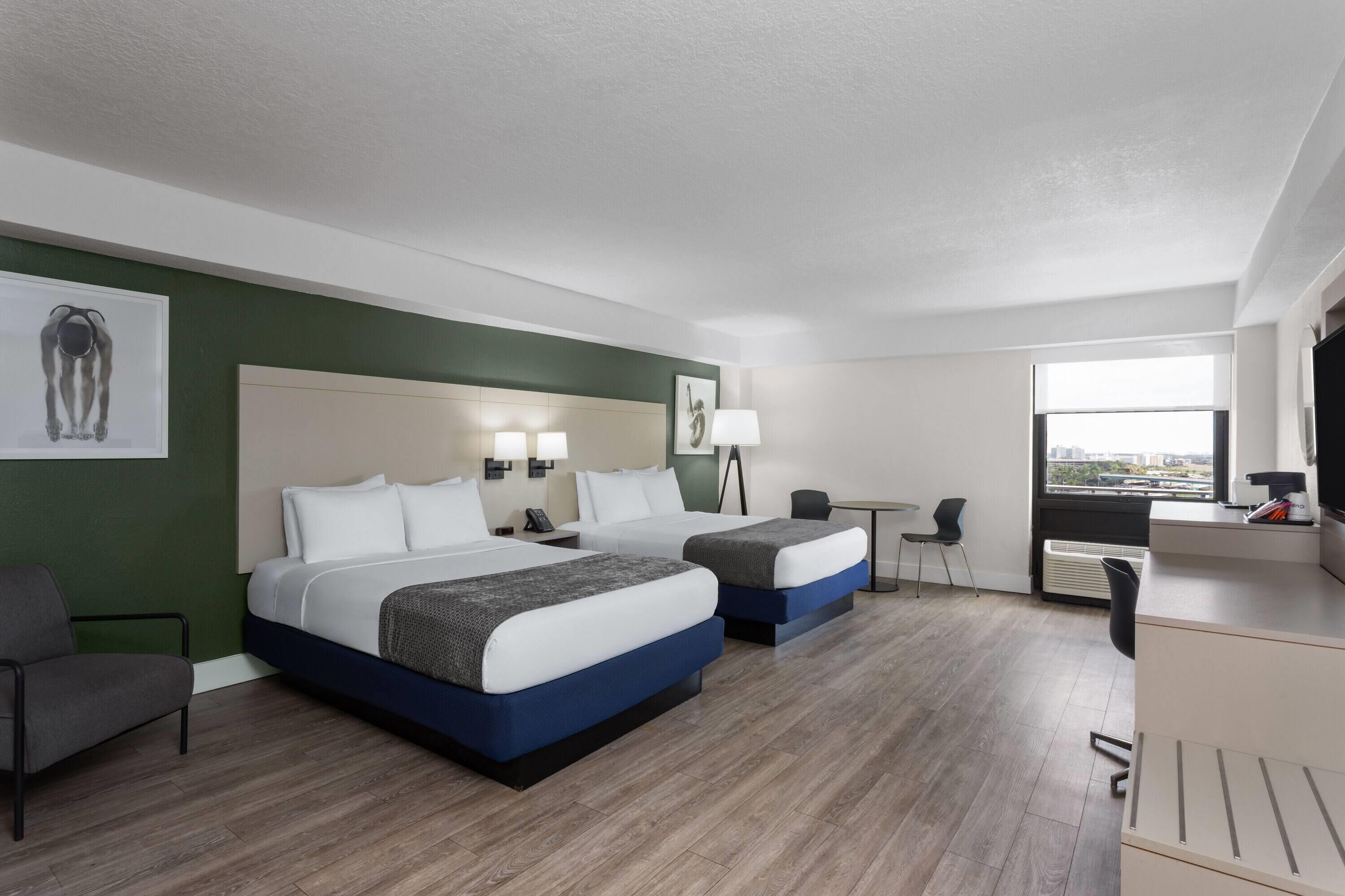 Een hotelkamer met twee bedden, een bureau, een stoel en een groot raam.