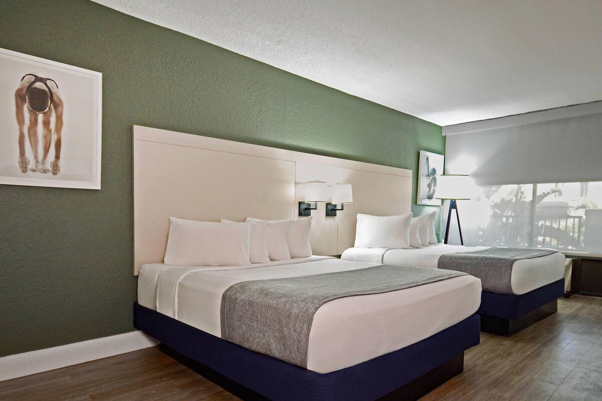 Una camera d'albergo con due letti, una parete verde e un'opera d'arte incorniciata.