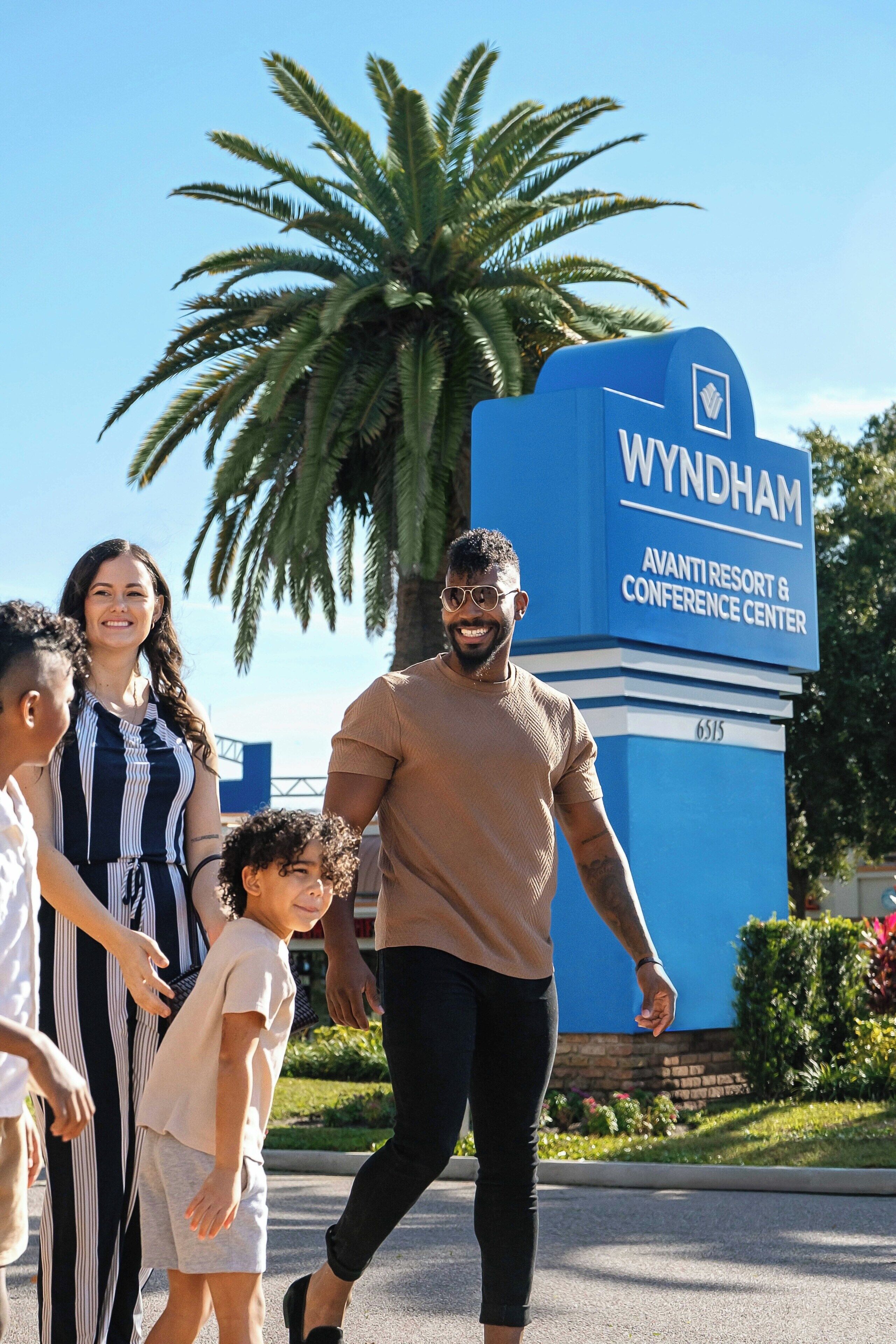 A family walking past a sign for Wyndham Avantis Resort & Conference Center.