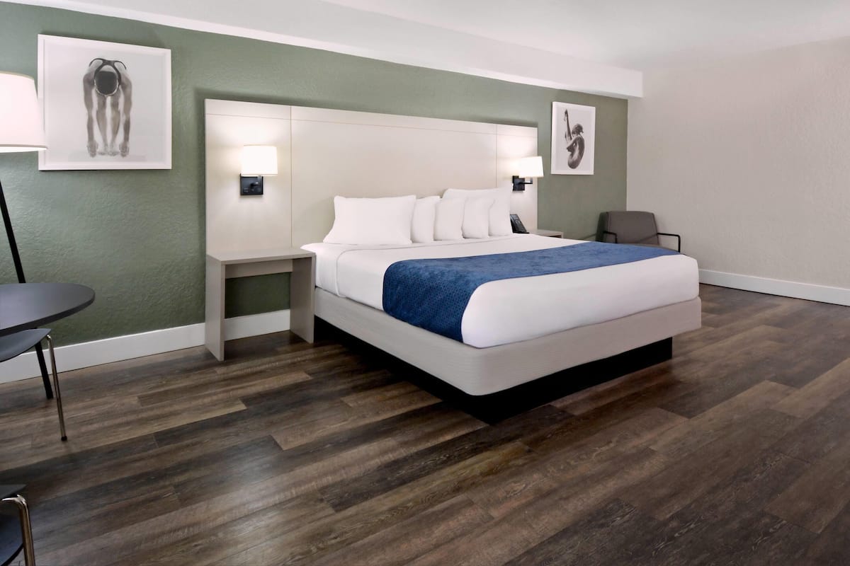 Una camera d'albergo con un letto, comodini, una sedia e opere d'arte alle pareti.