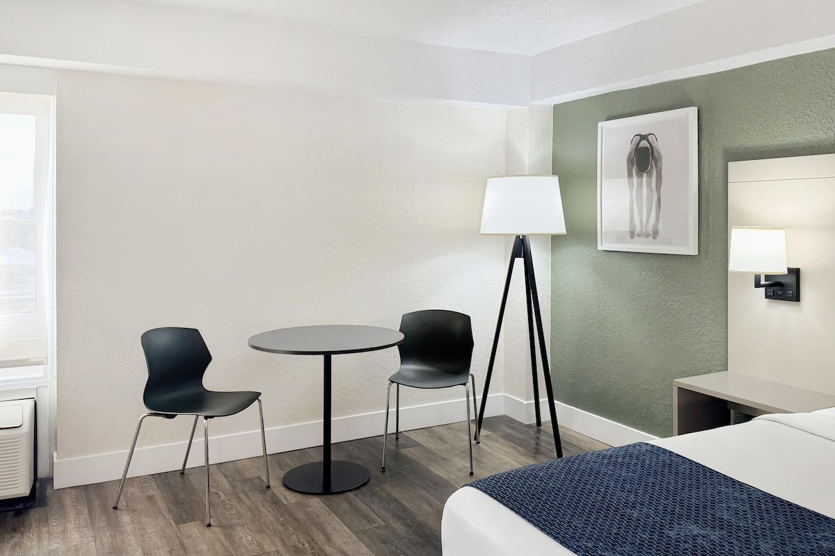 Una camera d'albergo con un letto, due poltrone, un tavolino, una lampada da terra e un quadro appeso al muro.
