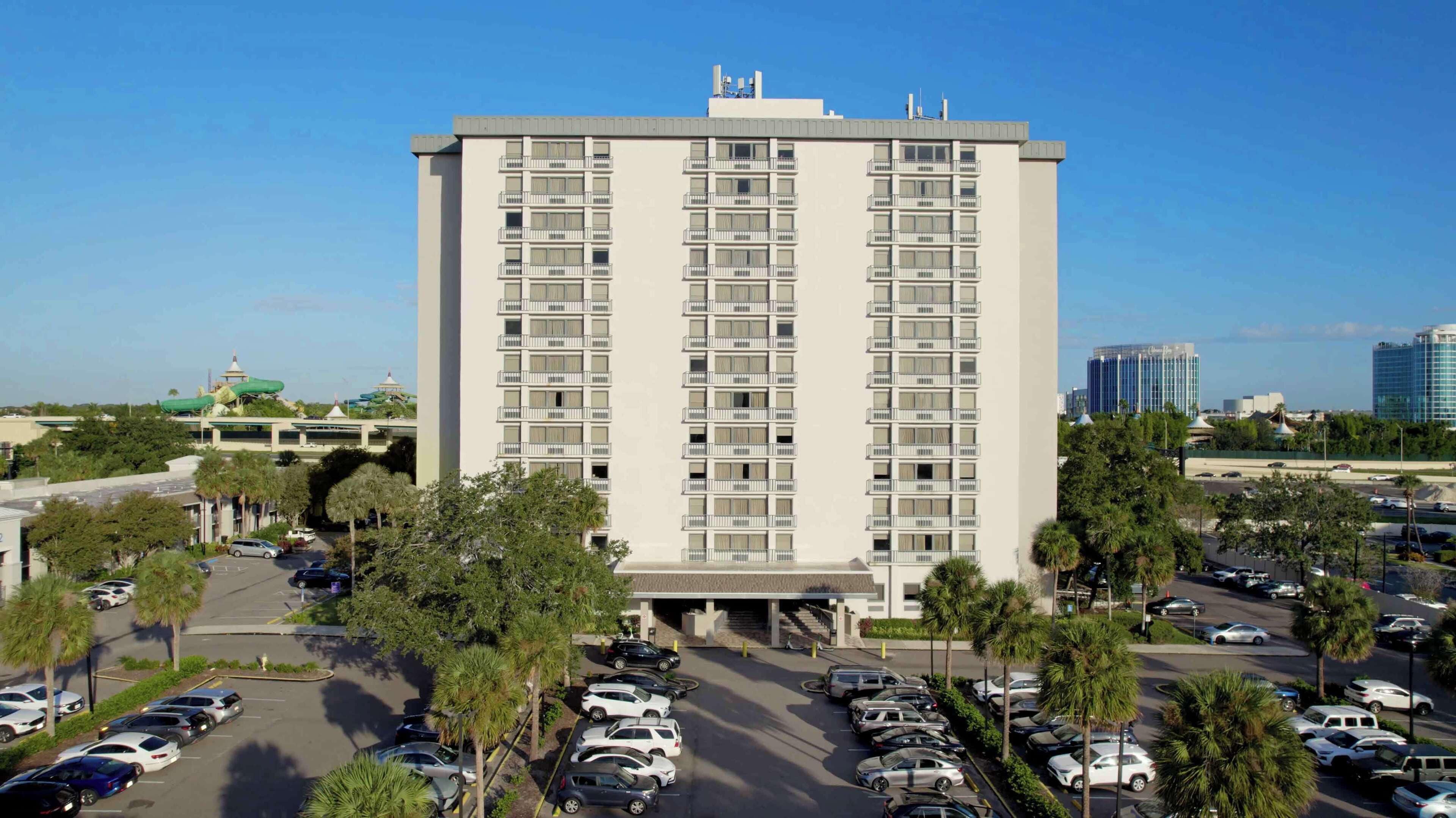 A multi-story hotel with a central entrance, surrounded by a parking lot with several cars.