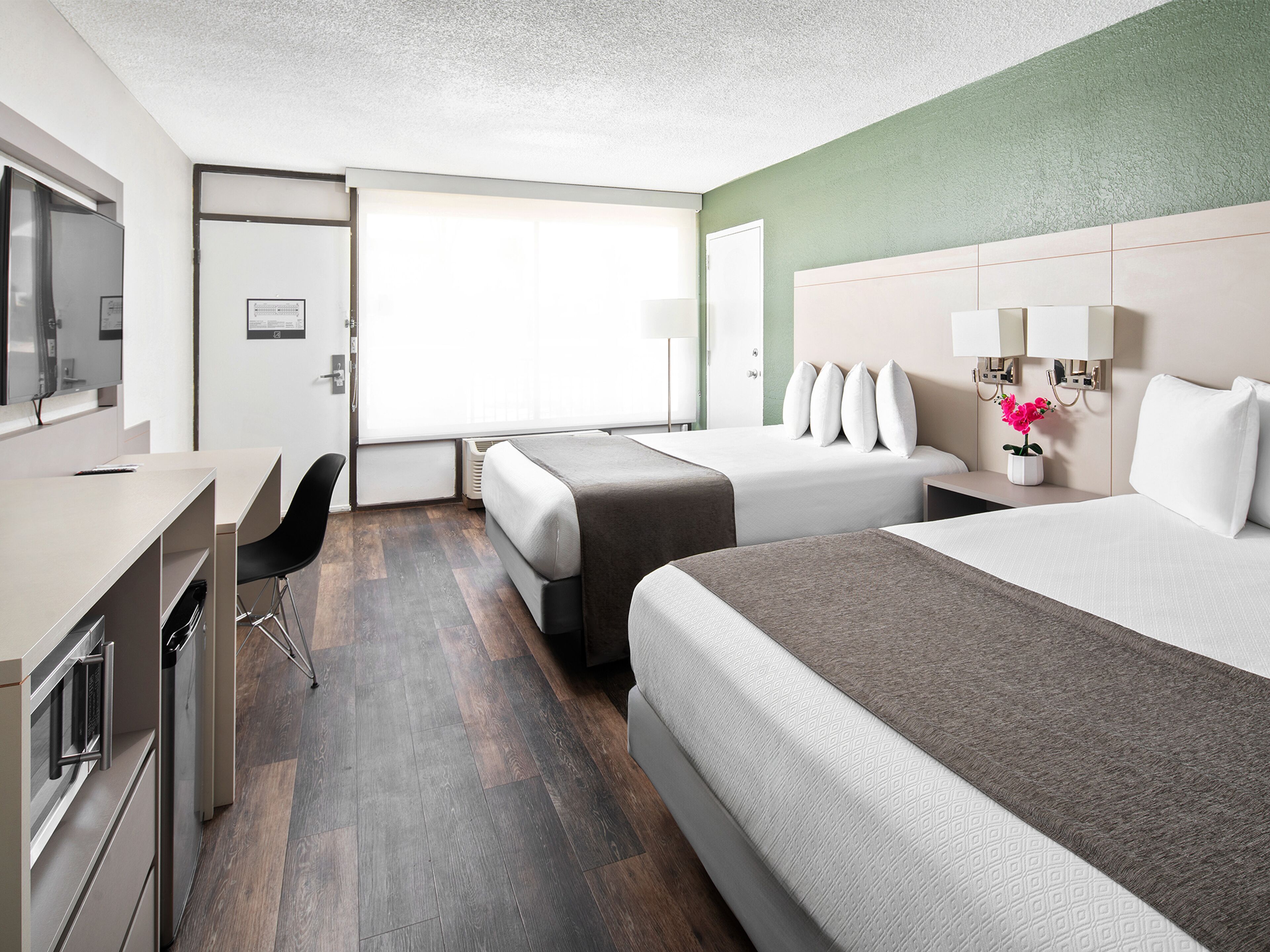 Een hotelkamer met twee bedden, een bureau, een stoel, een televisie en een raam.
