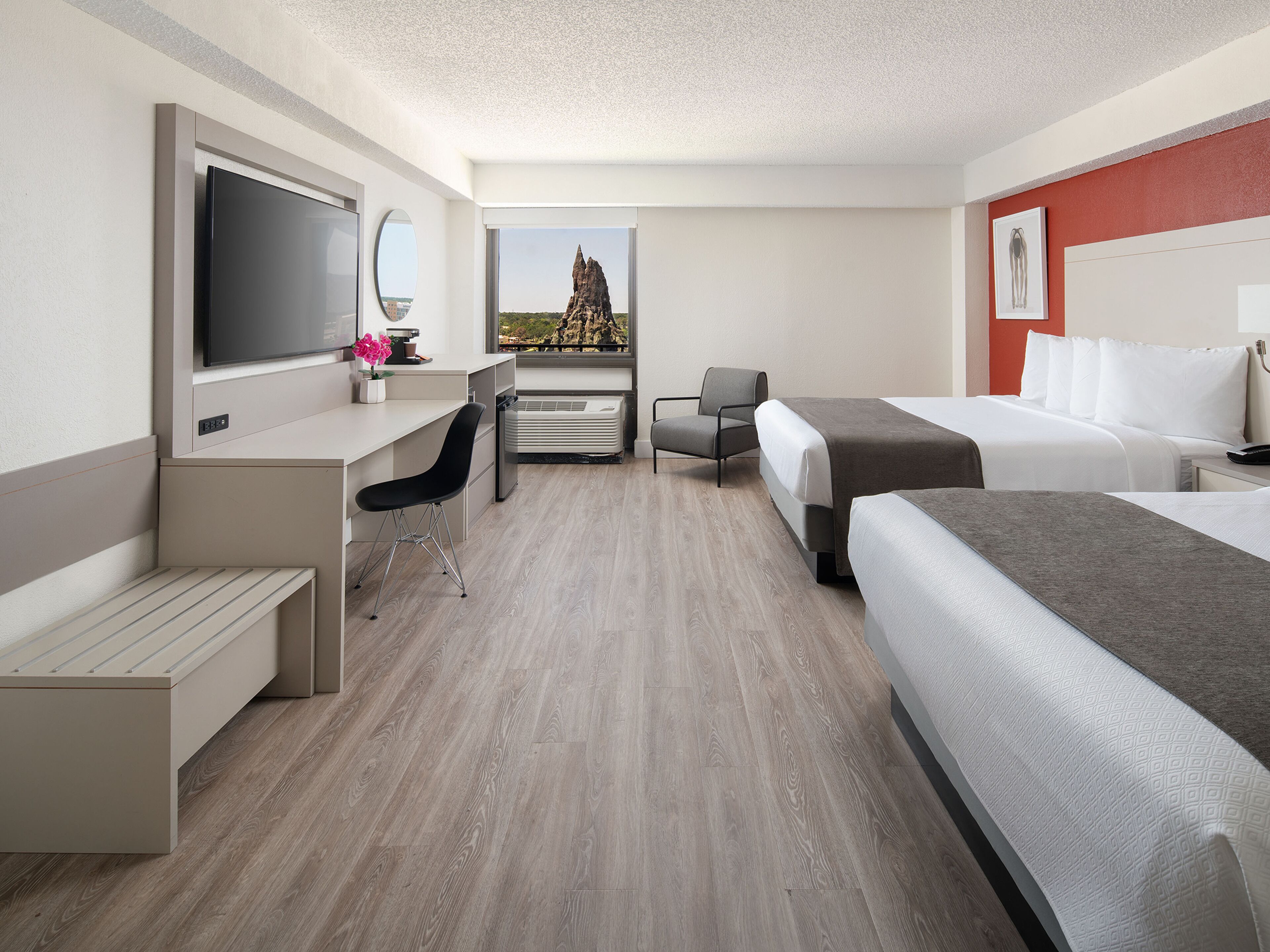 A hotel room with a bed, a desk with a chair, a TV, and a view of a mountain.