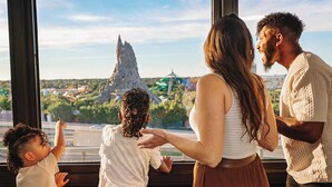 A family of four at a theme park, looking out a window at the park's attractions. - Wyndham I-Drive Avanti Resort & Conference Center (Orlando)
