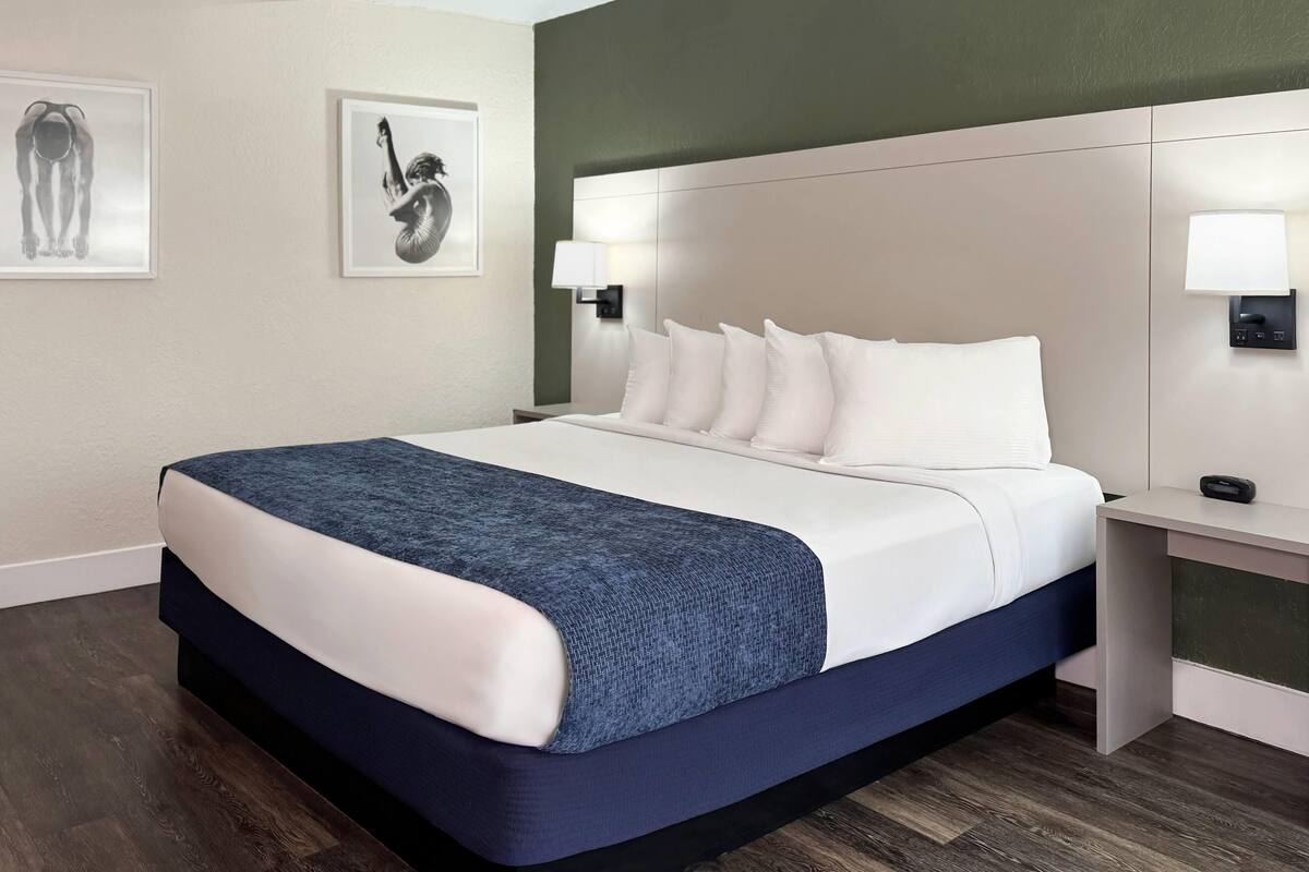 Un letto rifatto con cura, lenzuola bianche e blu, una testiera con illuminazione integrata e due opere d'arte incorniciate appese al muro.