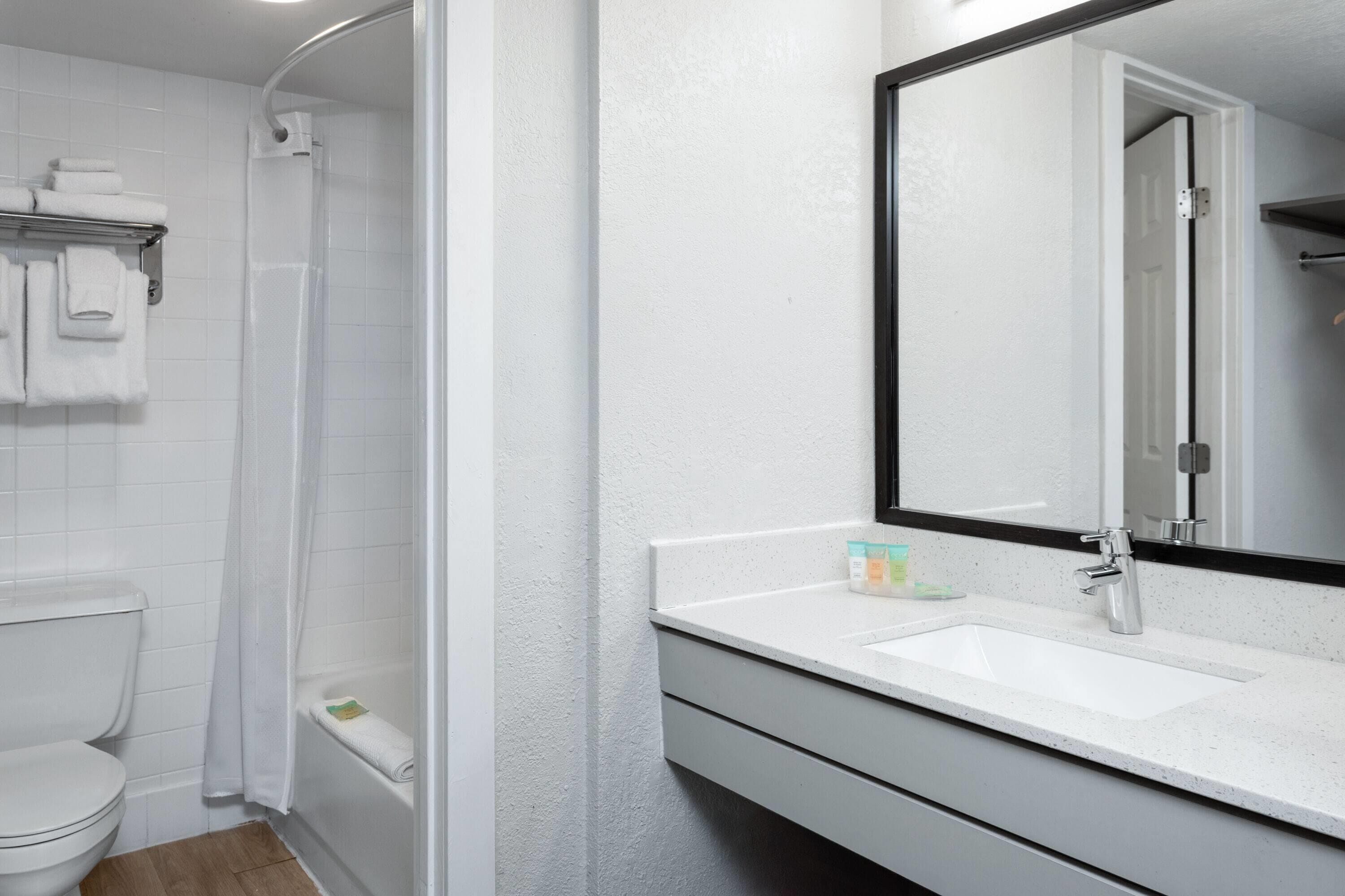 Une salle de bain avec des toilettes blanches, une douche, un lavabo avec un miroir et un porte-serviettes.