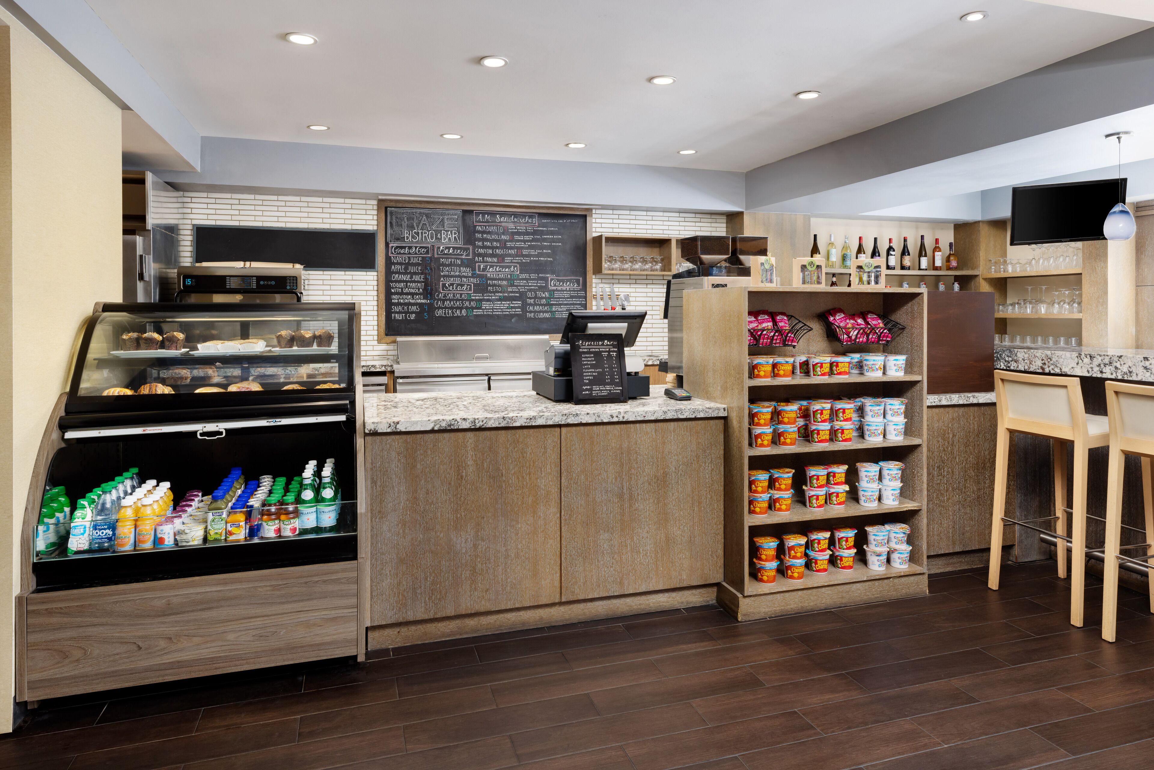 Un café moderno con una estación autoservicio para bebidas, un menú en pizarra y una variedad de aperitivos y condimentos.