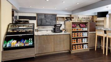 Un café moderno con una estación autoservicio para bebidas, un menú en pizarra y una variedad de aperitivos y condimentos.