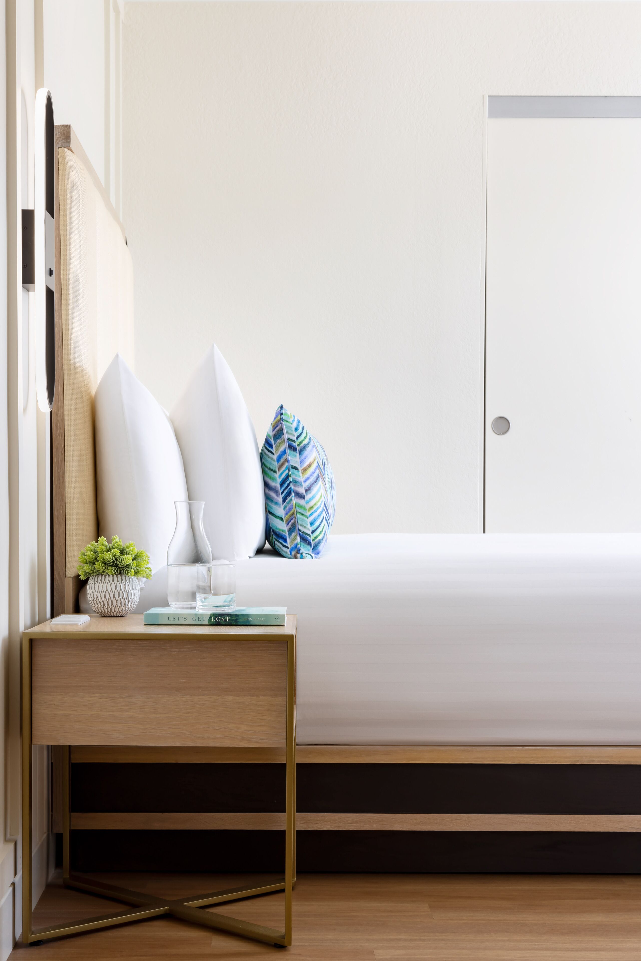 A neatly arranged bedroom with a bed, bedside table, and a small potted plant.