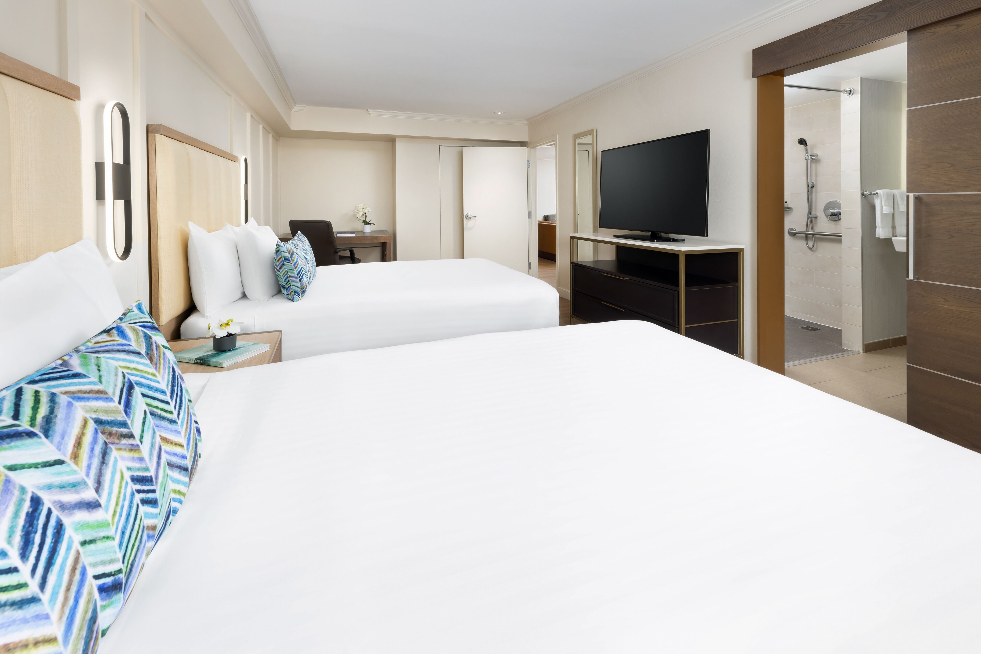 A hotel room with a large bed, a TV, a desk with a chair, and a shower area.
