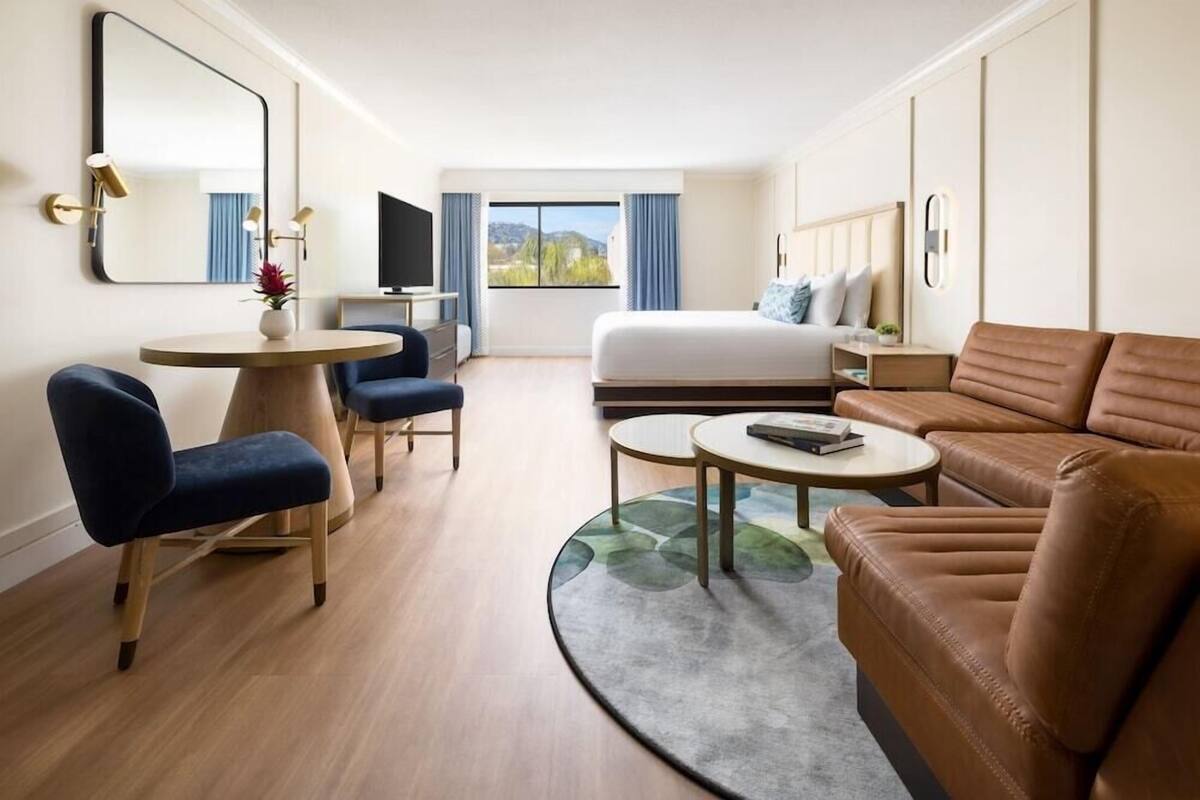 A hotel room with a bed, a sofa, a desk, a chair, a round table, and a TV.