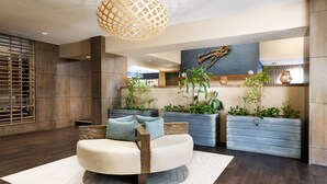 Un salón moderno con un sofá blanco redondeado, mesas auxiliares de madera y cojines azules. Hay plantas en macetas y una lámpara colgante grande de fibra.