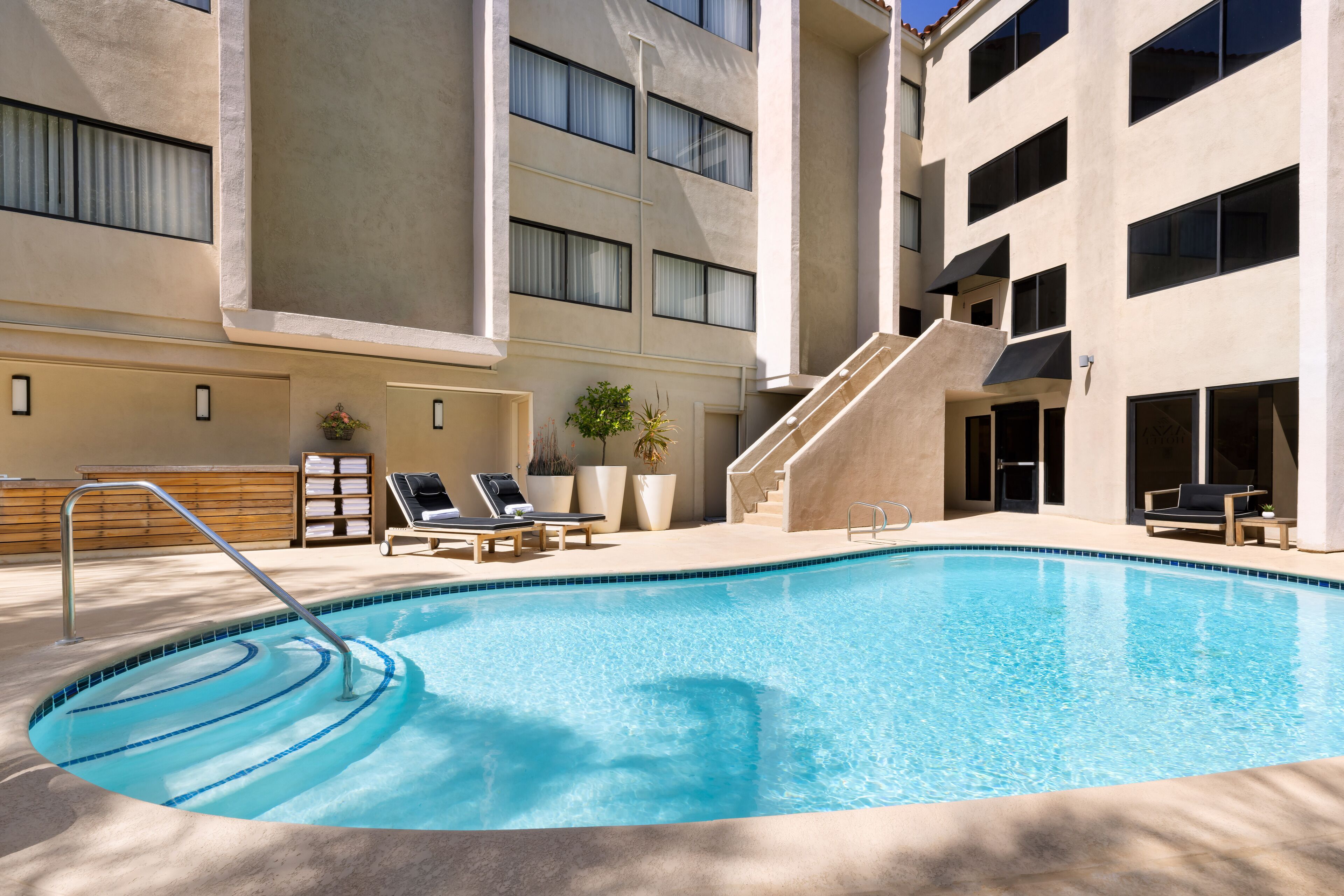 A swimming pool with a metal ladder, lounge chairs, and a staircase leading to an upper level.
