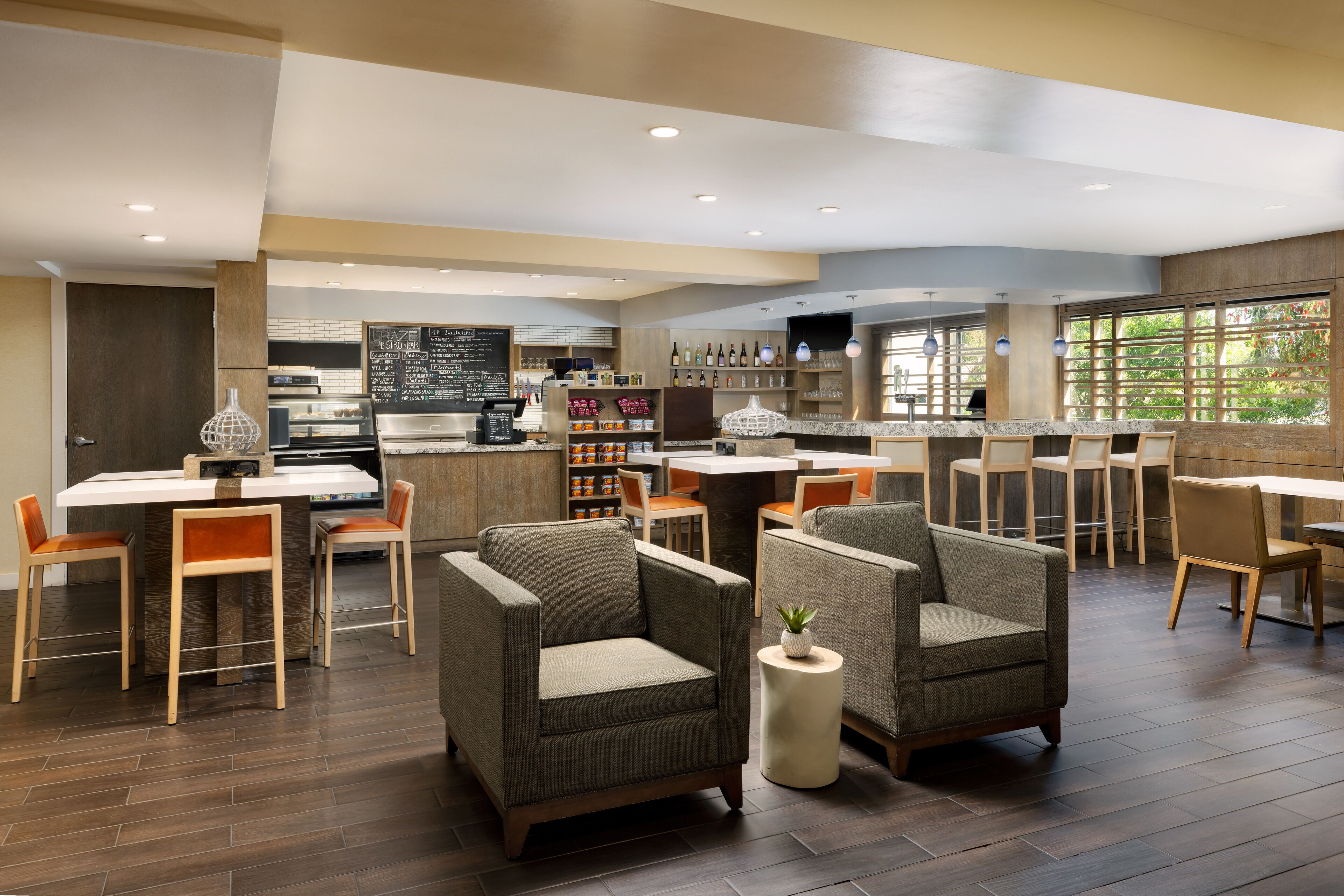A modern hotel lobby with a bar area, seating arrangements, and a kitchen in the background.