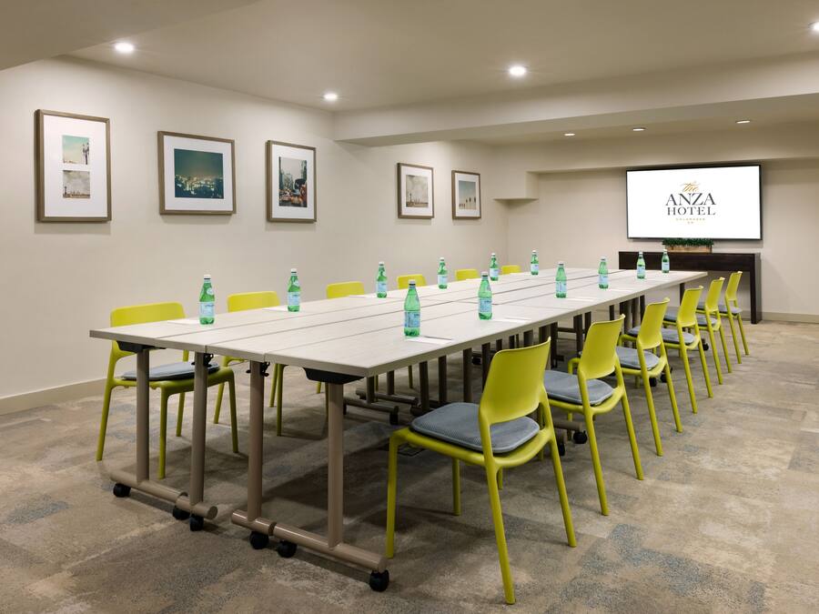 Une salle de conférence avec une longue table, des chaises jaunes et des bouteilles d’eau vertes.
