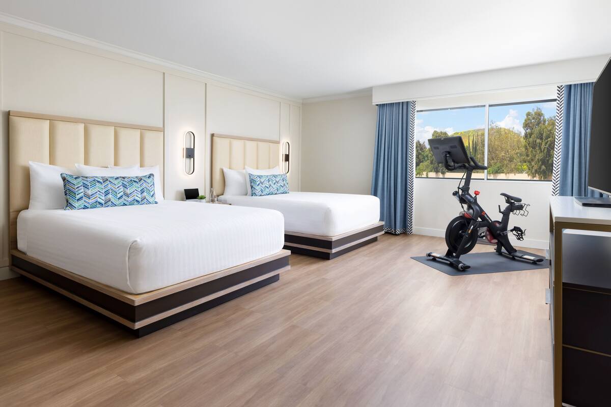 A hotel room with two beds, a desk, and an exercise bike.