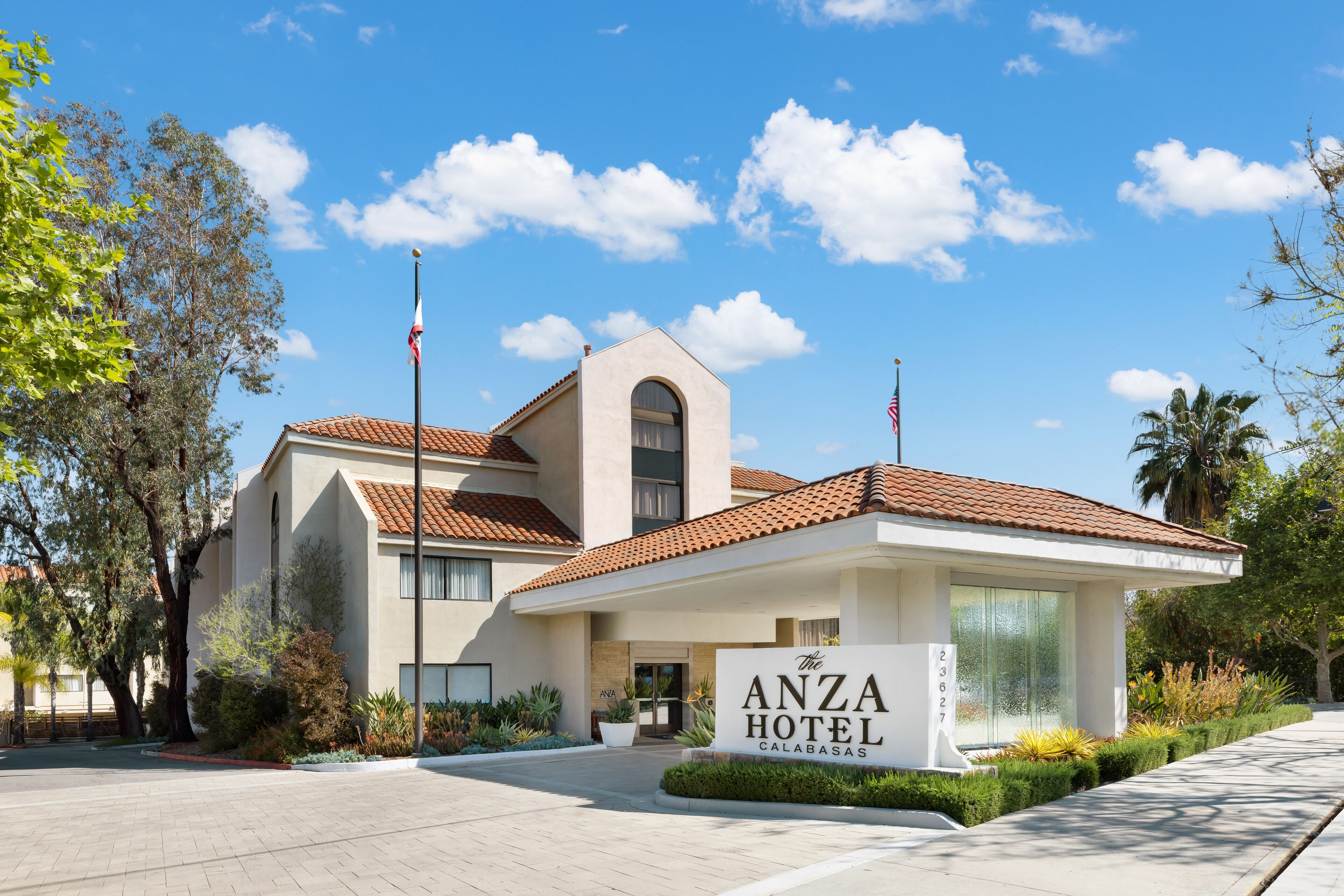 Hotel Anza, diseño moderno, con una entrada destacada, un asta de bandera y un jardín bien cuidado.