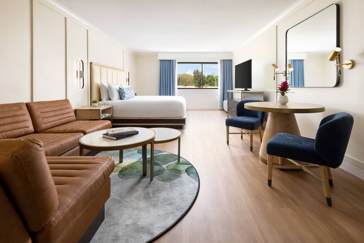 A hotel room with a bed, a sofa, a desk, a chair, and a round table.