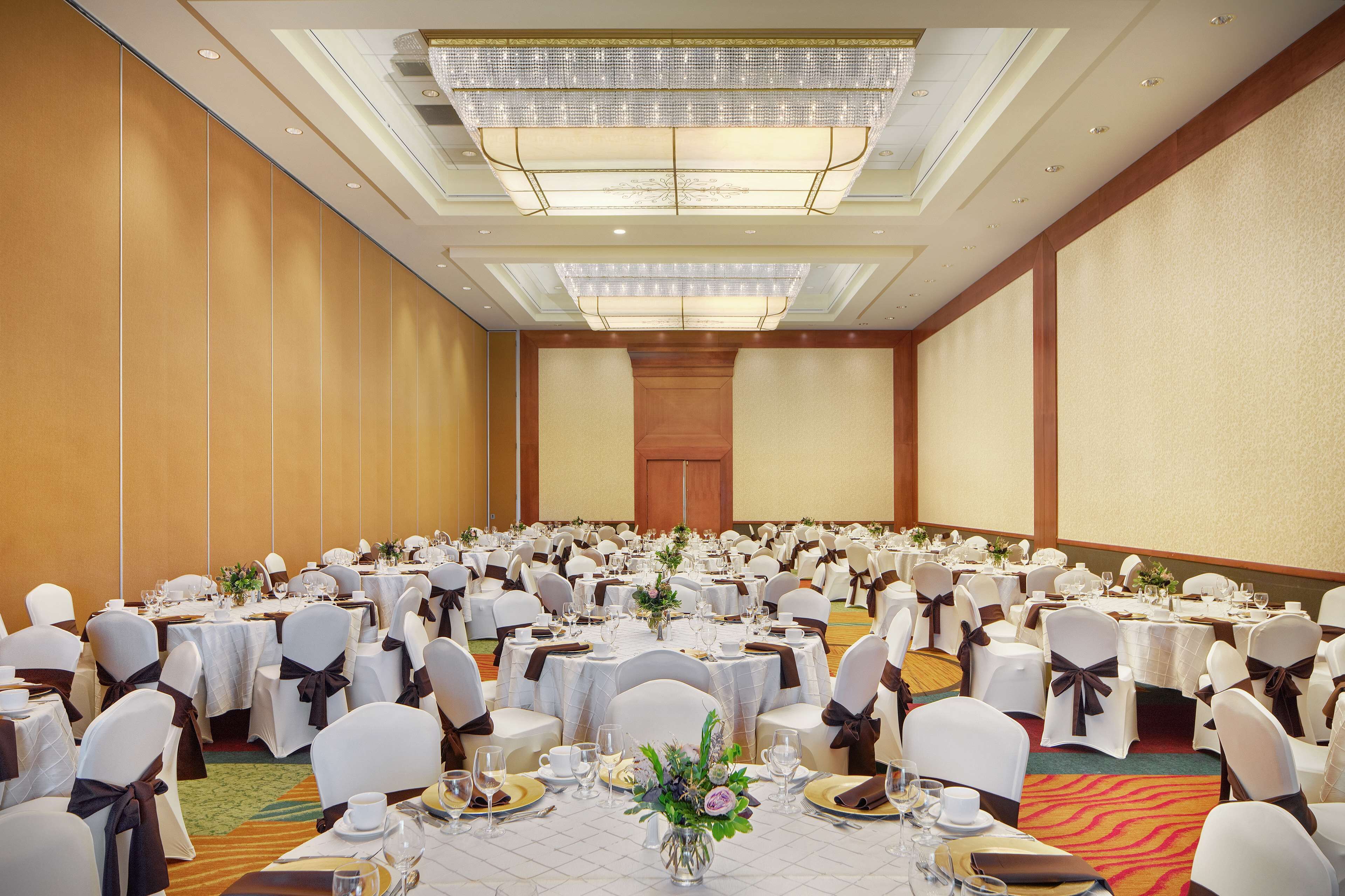 Un gran salón de banquetes con mesas redondas, sillas blancas y centros de mesa florales.