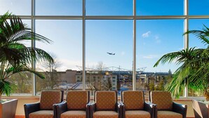 A seating area with a large window view of an airport and buildings. - Hilton Seattle Airport & Conference Center (SeaTac)