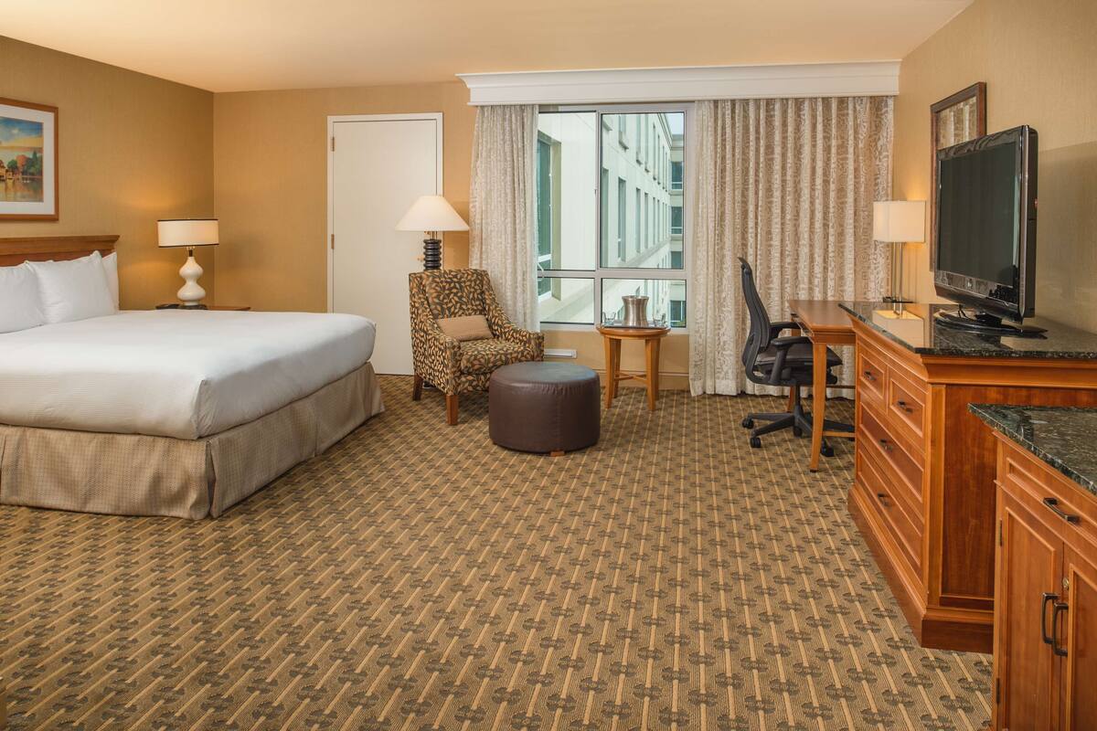 Une chambre d’hôtel avec un grand lit, une chaise, un bureau, une télévision et une fenêtre avec des rideaux.