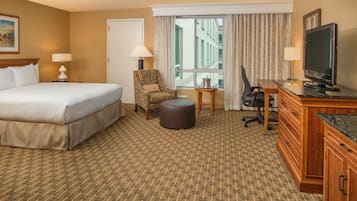 A hotel room with a large bed, a chair, a desk, a television, and a window with curtains.