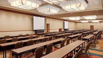 A conference room with rows of tables and chairs, a large screen, and a projector.