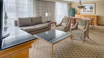 Habitación de hotel con sofá, sillones, mesa de comedor y televisor.