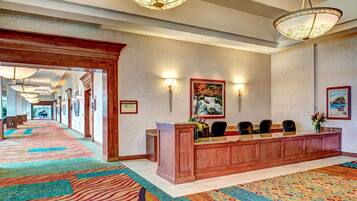 A hotel lobby with a reception desk, chairs, and a patterned carpet.