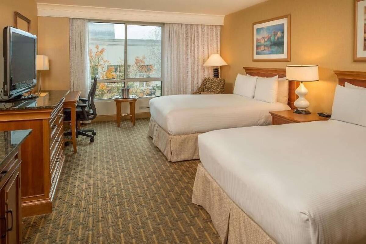 Ein Hotelzimmer mit zwei Betten, einem Schreibtisch mit Fernseher, einem kleinen Tisch und einem Fenster mit Blick.
