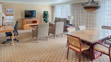 Une chambre d’hôtel comprenant un lit, une télévision, une table à manger avec des chaises, un canapé et une grande fenêtre avec des rideaux.