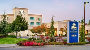 A Hilton Seattle Airport & Conference Center building with a sign, surrounded by landscaped gardens and trees. - Hilton Seattle Airport & Conference Center (SeaTac)