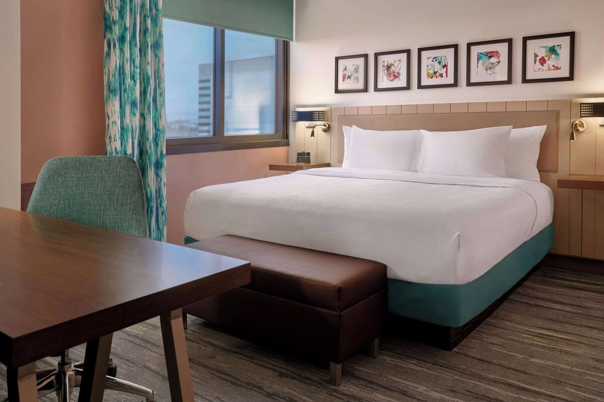 Une chambre d’hôtel avec un lit, un bureau, une chaise et une fenêtre avec des rideaux.
