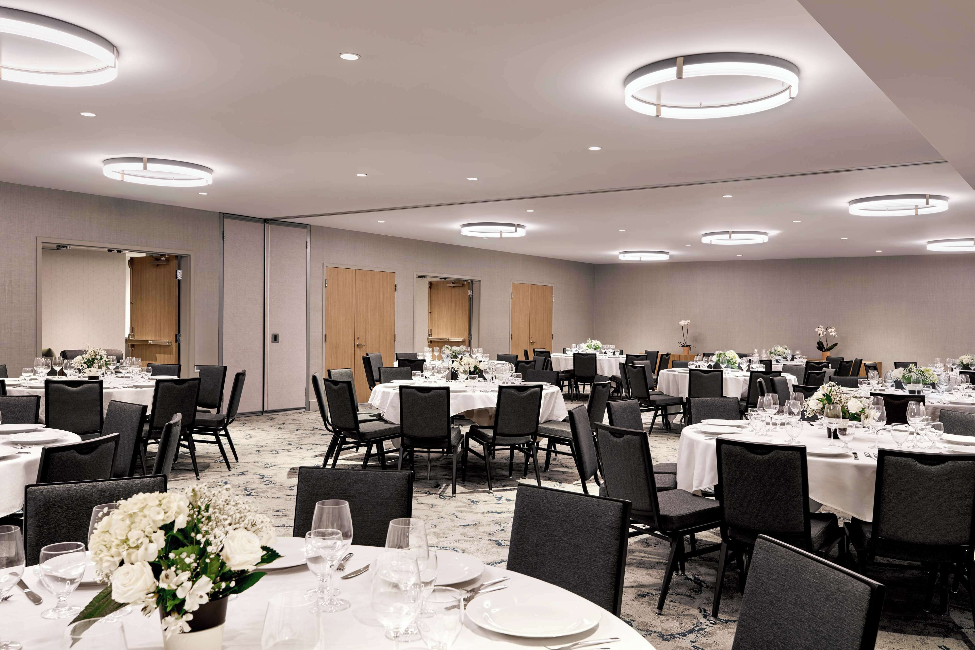 A large banquet hall with multiple round tables set for dining, equipped with chairs and table settings.