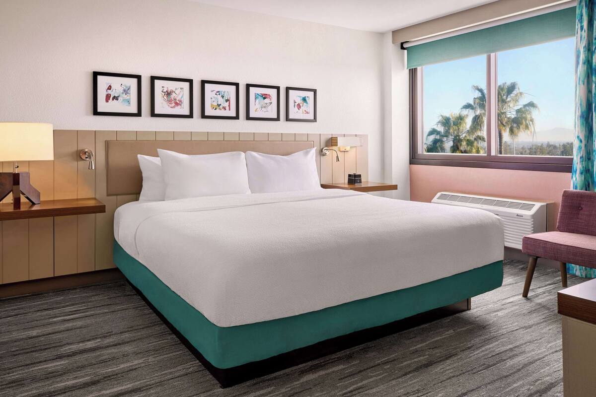 Une chambre d’hôtel avec un grand lit, une table de chevet, une chaise et une fenêtre donnant sur des palmiers.