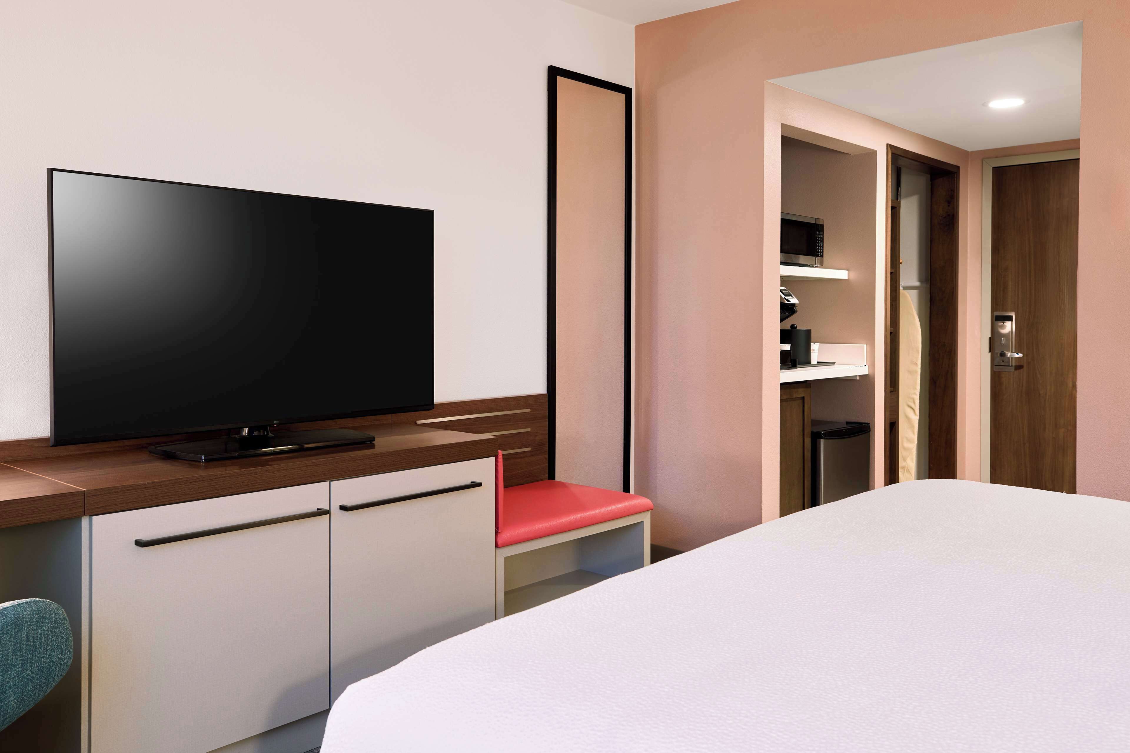 A hotel room with a bed, a TV on a wooden cabinet, a red chair, and a wardrobe.