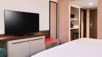A hotel room with a bed, a TV on a wooden cabinet, a red chair, and a wardrobe.