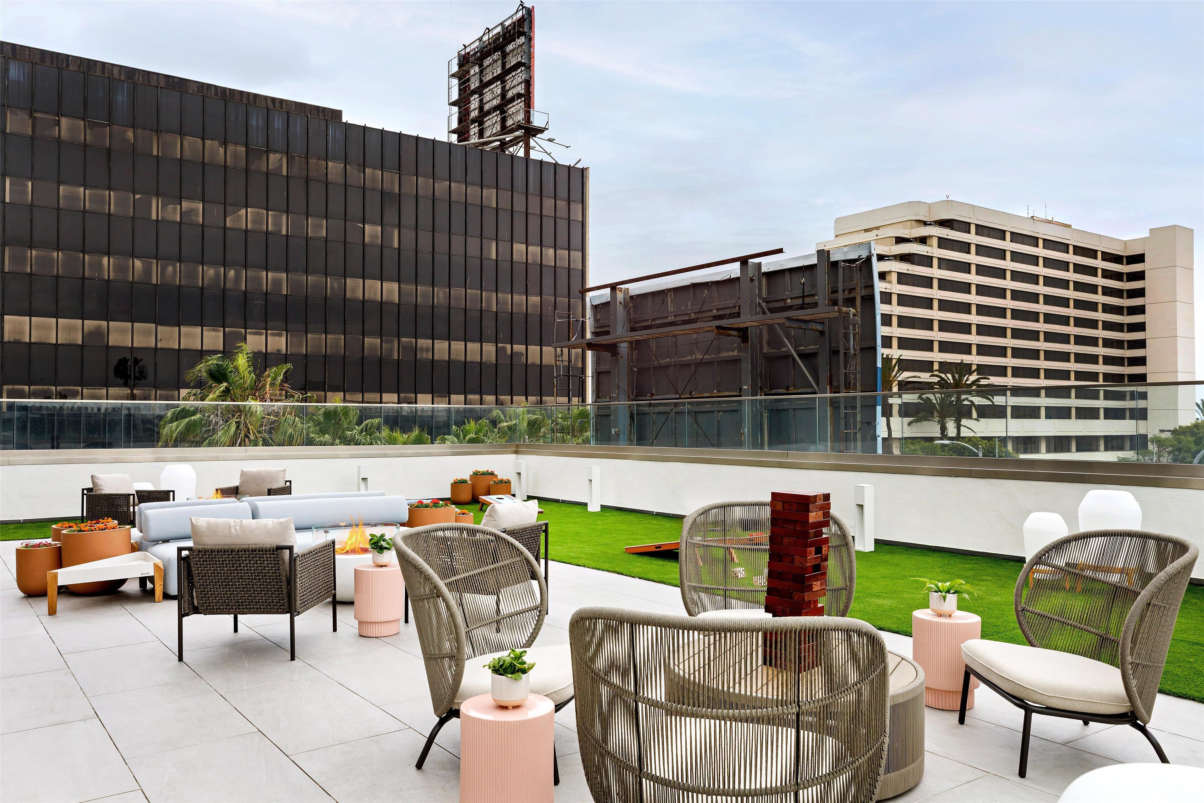 Una terraza en la azotea con mobiliario de mimbre, un pequeño jardín y vistas de los edificios circundantes.