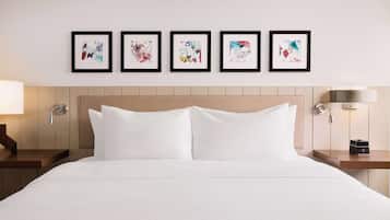 Een hotelkamer met een groot bed, twee nachtkastjes, een wandlamp, een thermostaat, en vijf ingelijste kunstwerken boven het bed.