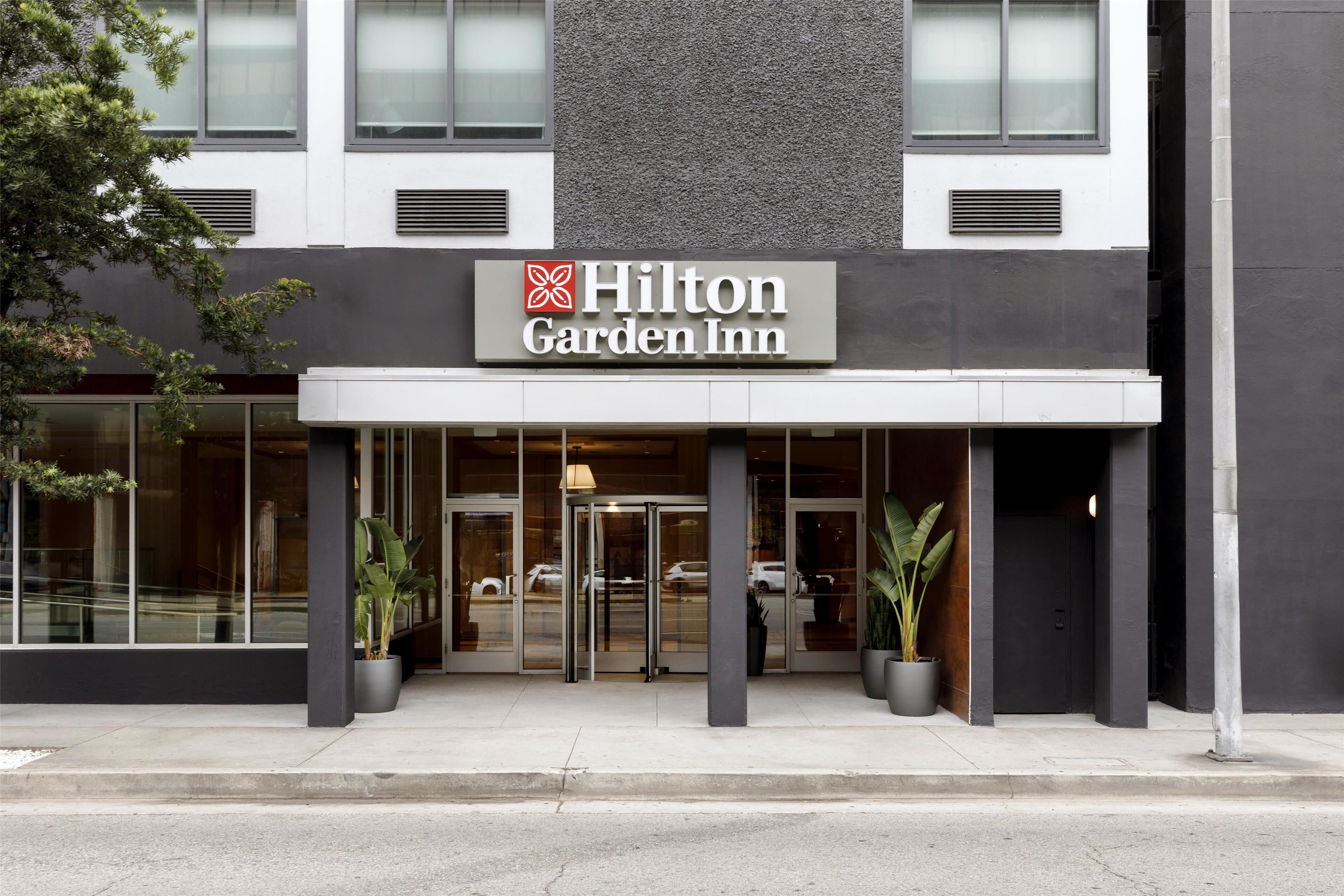 The exterior of a Hilton Garden Inn with a modern facade, large glass windows, and a prominent entrance with a revolving door.