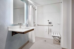 Een moderne badkamer met een wastafel, spiegel, douche en handgrepen.