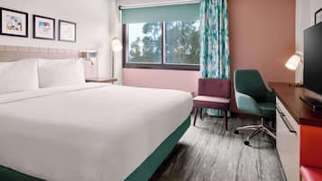 A hotel room with a bed, a desk with a chair, a TV, and framed artwork on the wall.
