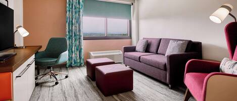 A hotel room with a desk, a green chair, a purple sofa, and a red armchair.
