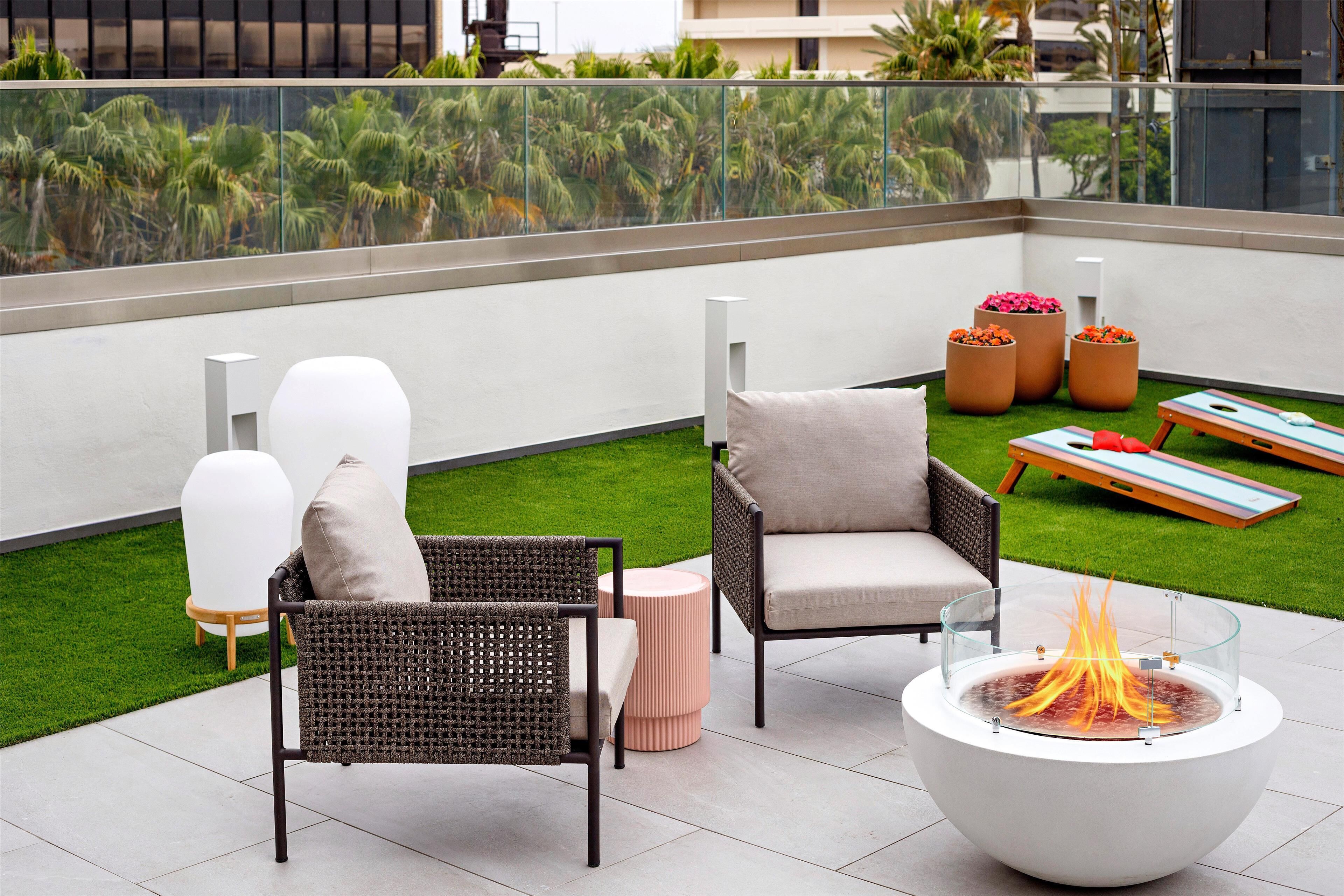 Una terraza en la azotea con dos sillones de mimbre, una mesa redonda con superficie de vidrio y una chimenea pequeña.