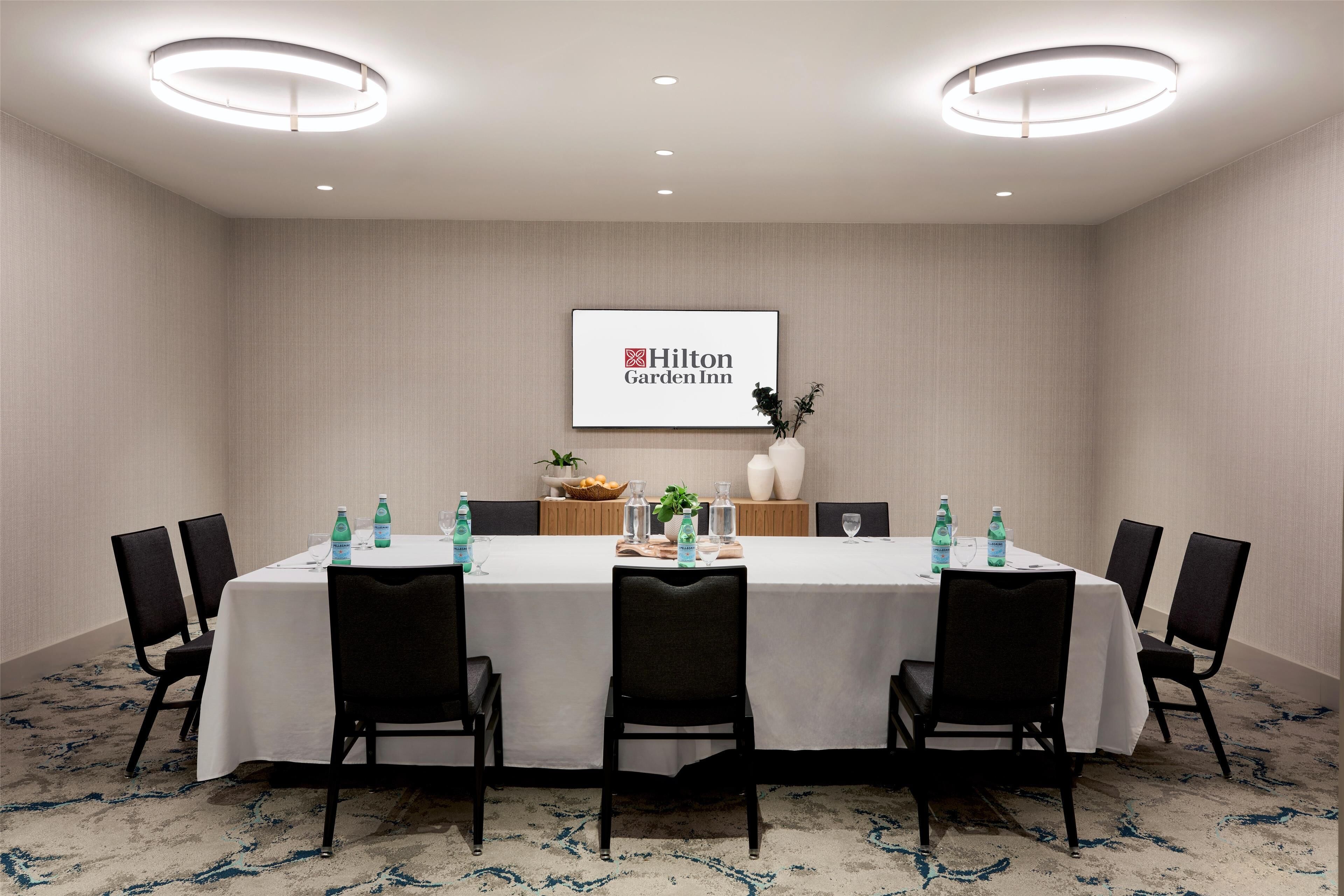 A conference room with a long table, black chairs, a white tablecloth, and a Hilton Garden Inn logo on the wall.