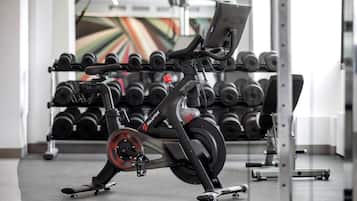 Un vélo d’appartement dans une salle de sport, avec un porte-haltères en arrière-plan.