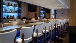 Una zona de bar moderna con múltiples estantes llenos de botellas de licor, una barra larga con taburetes y un diseño limpio y contemporáneo.