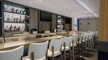 A modern bar area with a long counter, multiple seating options, and a variety of liquor bottles on shelves.
